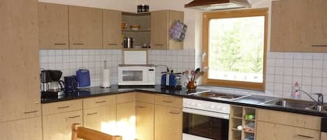 A compact kitchen with wooden cabinets, a microwave, a stove, and a window providing natural light.