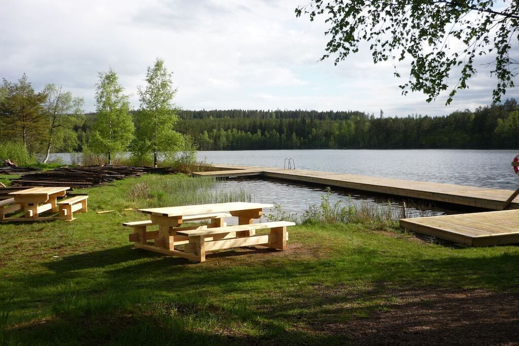 A lakeside picnic area with wooden benches and a dock extending into the water.