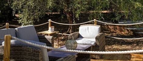 A wicker outdoor seating area with a rope barrier, surrounded by trees.