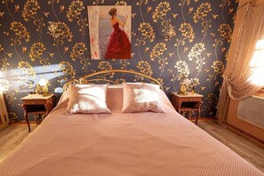 Ein Schlafzimmer mit einem großen Bett, zwei Nachttischen, einem Bild an der Wand und floralem Wandpapier.