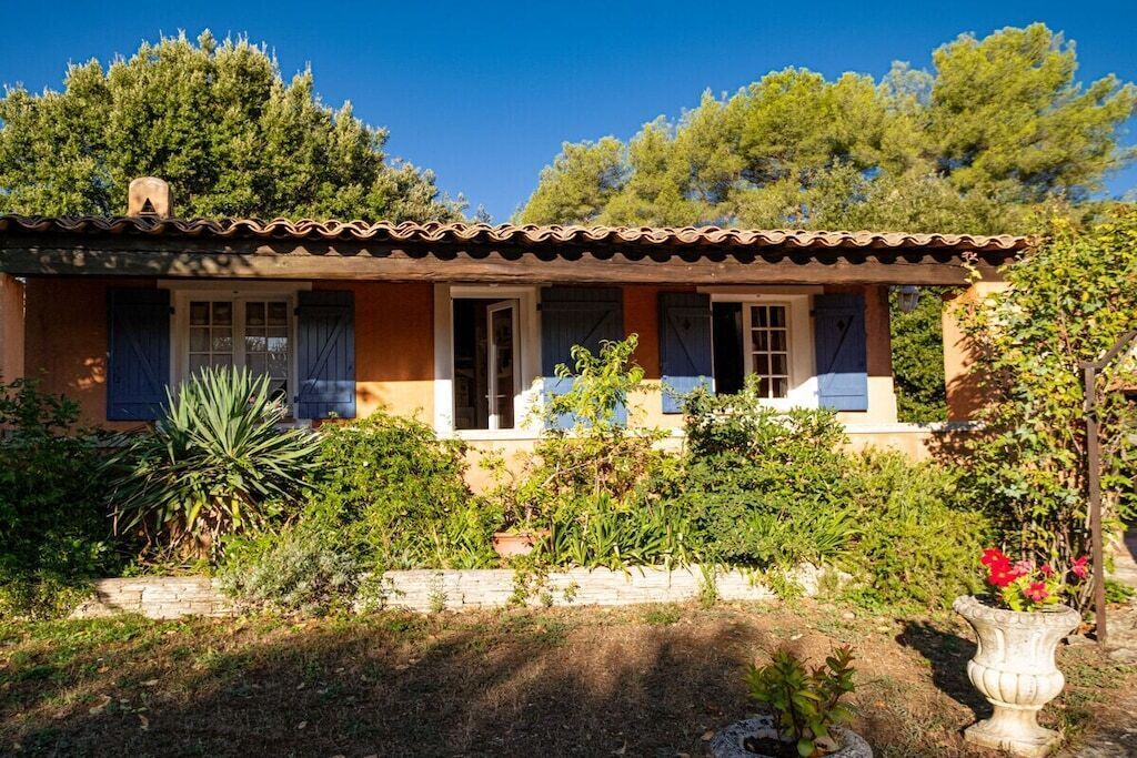 Een huis in traditionele Mediterrane stijl, met een pannendak, een tuin vol planten en een helderblauwe lucht.