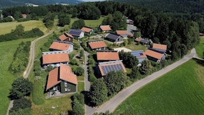 Vue aérienne d’un quartier résidentiel avec des maisons, dont certaines sont équipées de panneaux solaires, entouré de verdure et de collines.