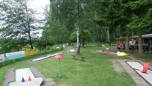 Un espace extérieur comprenant un terrain d’entraînement au putting, des tables de pique-nique et des parasols.