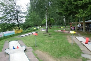 Ein Außenbereich mit Putting Green, Picknicktischen und Sonnenschirmen.