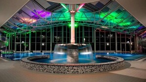 Un espace piscine intérieur moderne, doté d’un élément aquatique central et d’une structure de plafond en verre.