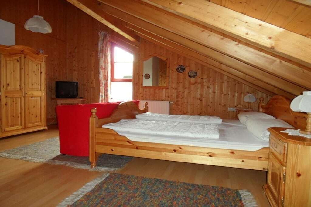 Quarto de madeira com cama, televisão e uma cadeira vermelha.
