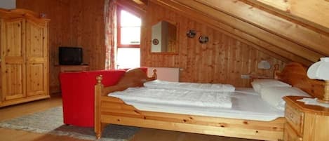 A wooden room with a bed, a television, and a red chair.
