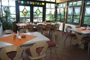 Un restaurant doté de nombreuses tables et chaises, de grandes fenêtres offrant une vue dégagée et d’un sol carrelé.