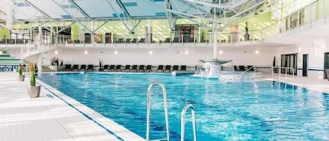 An indoor swimming pool with clear water, a diving board, and a staircase leading to an upper level.