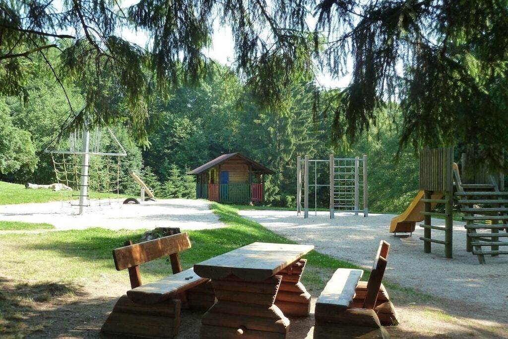 A picnic area with benches and a table, surrounded by trees and a playground.