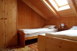 Une pièce en bois avec un plafond en pente, deux lits, une table de chevet et une fenêtre.