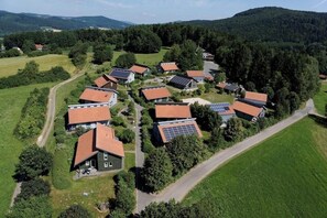 Vue aérienne d’un quartier résidentiel avec des maisons, dont certaines sont équipées de panneaux solaires, entouré de verdure et de collines.
