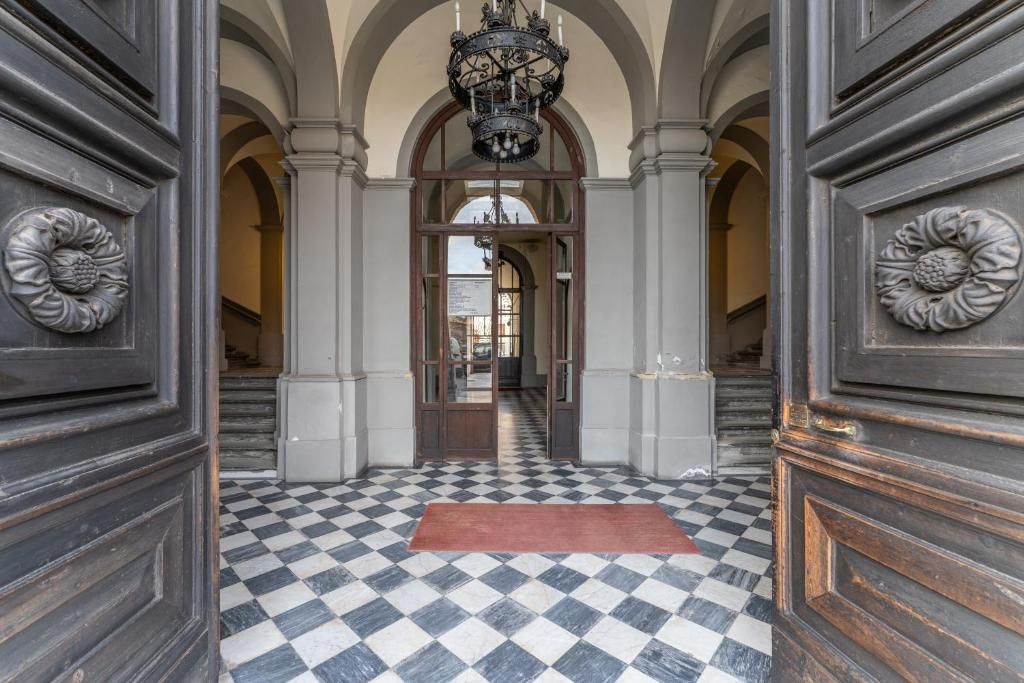 Un couloir doté d’un sol à carreaux, d’arcades et d’un lustre.