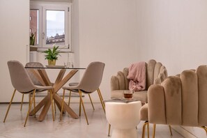 Uma sala de jantar moderna com mesa de vidro, duas cadeiras e um sofá com manta rosa.