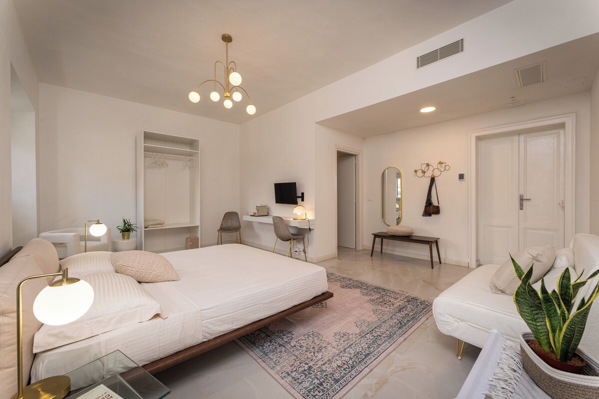A spacious bedroom with a large bed, bedside tables, a desk, and a chair.