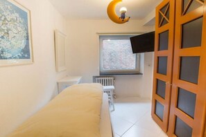 Ein Schlafzimmer mit einem Bett, einem Fenster, einer Heizung, einem Fernseher und einer Tür.