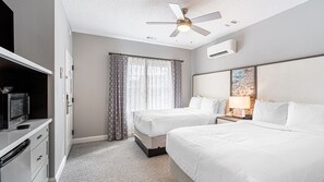 A hotel room with two beds, a ceiling fan, an air conditioning unit, a desk with a microwave, and a window with patterned curtains. - Myrtle Beach | Beach Escape | Pool & Boardwalk | Hotel (Myrtle Beach)