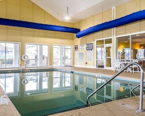An indoor swimming pool with clear glass walls, a blue ceiling, and a seating area with white chairs. - Myrtle Beach | Beach Escape | Pool & Boardwalk | Hotel (Myrtle Beach)