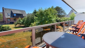 Varanda com mesa e cadeiras, com vista para um gramado e casas vizinhas.