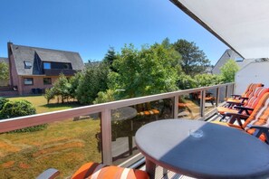 Ein Balkon mit Tisch und Stühlen, der auf einen Rasen und angrenzende Häuser blickt.