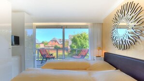 Quarto de hotel com uma cama grande, televisão, varanda com cadeiras e um objeto decorativo na parede.