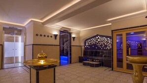 Um hall com piso xadrez, uma tigela dourada decorativa, uma área de estar com sofá preto e uma parede com padrão de estrelas.