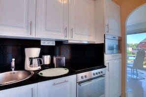 A modern kitchen with white cabinets, a black countertop, and stainless steel appliances including a coffee maker, toaster, and oven. - Holiday apartment in Sylt with 1 bedroom (Wenningstedt)