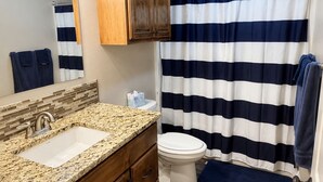 Un bagno con un mobile lavabo in legno, un lavandino bianco, un WC e una tenda da doccia a righe.