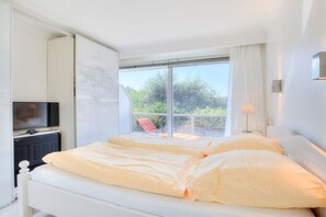 Ein Hotelzimmer mit einem Bett, einem Fernseher, einem Fenster mit Blick auf Grünflächen und einem Stuhl draußen.
