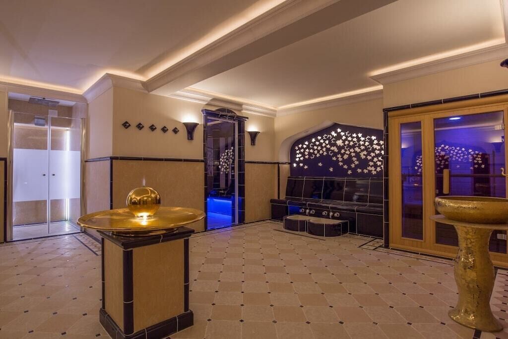 A spacious lobby with a modern design, featuring a central seating area, a decorative wall with a star pattern, and a large golden fountain.