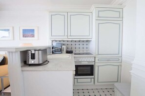 Une cuisine de taille réduite avec des meubles blancs, un grille-pain, une bouilloire et une cuisinière.