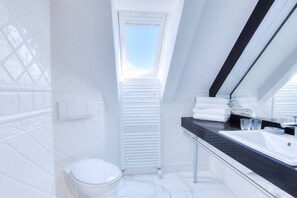 Une salle de bain moderne avec un puits de lumière, des carreaux blancs, des toilettes blanches et un plan de toilette noir avec un lavabo.