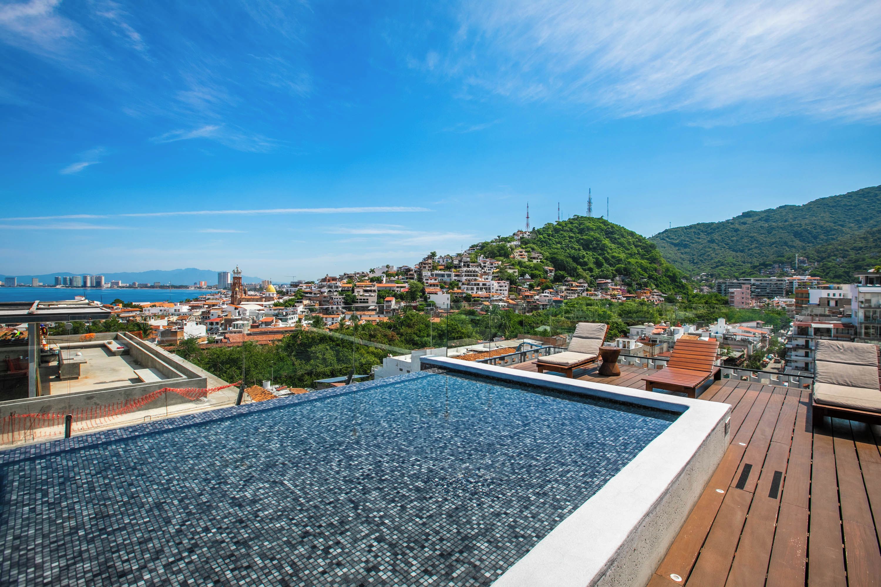 A rooftop pool with a view of a coastal cityscape and a hill with buildings.