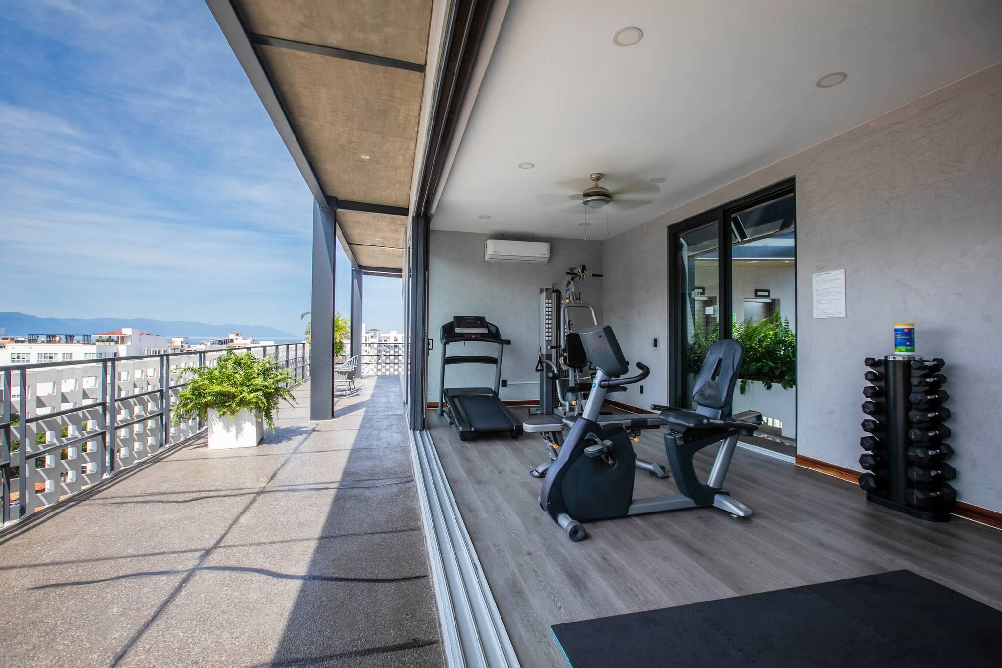 A balcony with exercise equipment, a view of the city, and a potted plant.