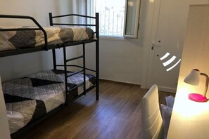 Et værelse med køjeseng, skrivebord med lampe og et vindue med persienner.