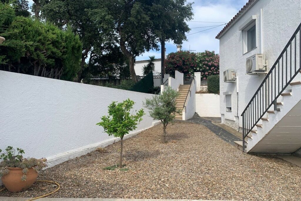 Un immeuble résidentiel à la façade blanche, avec une allée en gravier, un petit arbre et un escalier menant à un étage supérieur.