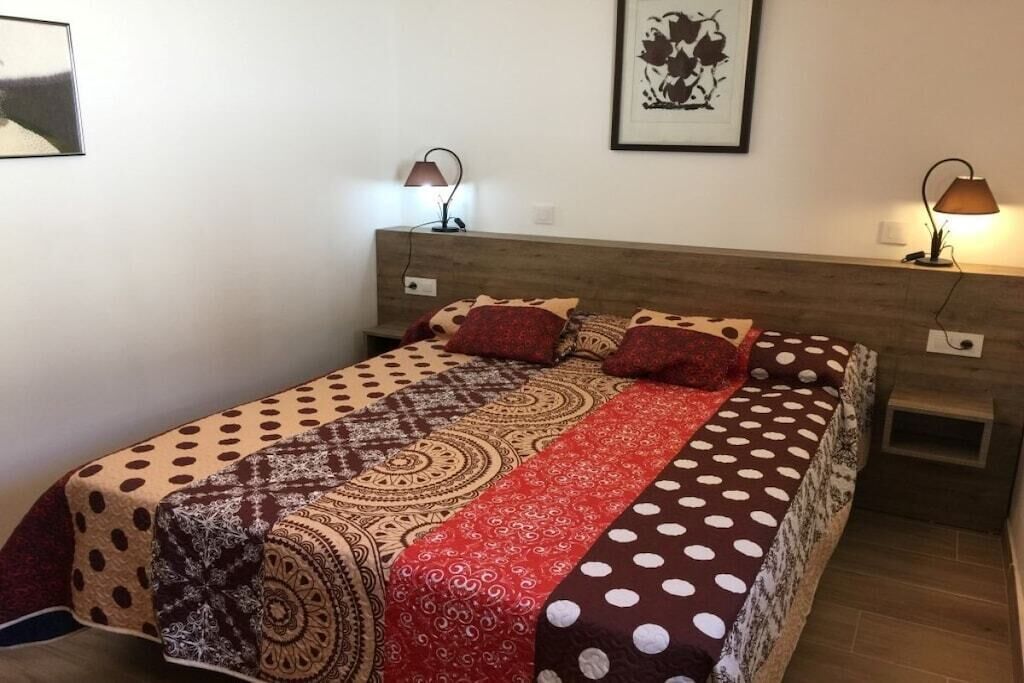 Ein Schlafzimmer mit einem Bett, zwei Nachttischlampen, einem gerahmten Bild an der Wand und einem kleinen Nachttisch.