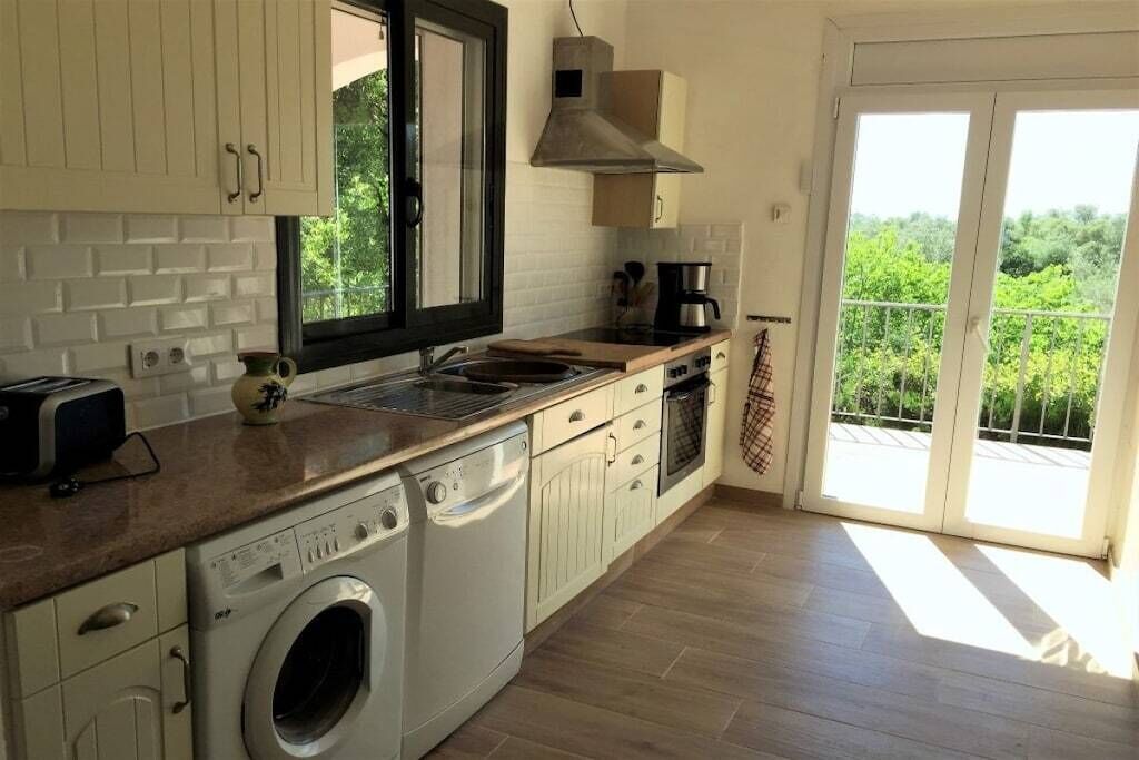 A kitchen with a washing machine, a coffee maker, and a view of greenery through the window.