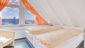 Quarto com duas camas, janela com cortinas, escrivaninha e uma cadeira.