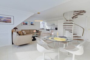 Un salon moderne avec une table à manger en verre, des canapés blancs et un escalier en colimaçon.
