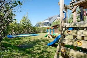 Une structure de jeu en bois avec des toboggans et des éléments d’escalade, un toboggan bleu et une petite maison de jeu dans un jardin.