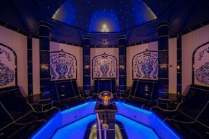 Una habitación lujosa con piscina central, diseños ornamentales en las paredes y un techo estrellado.
