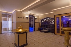 Un hall con mostrador de recepción, una pared decorativa con diseño floral y una zona de estar con fondo iluminado en azul.