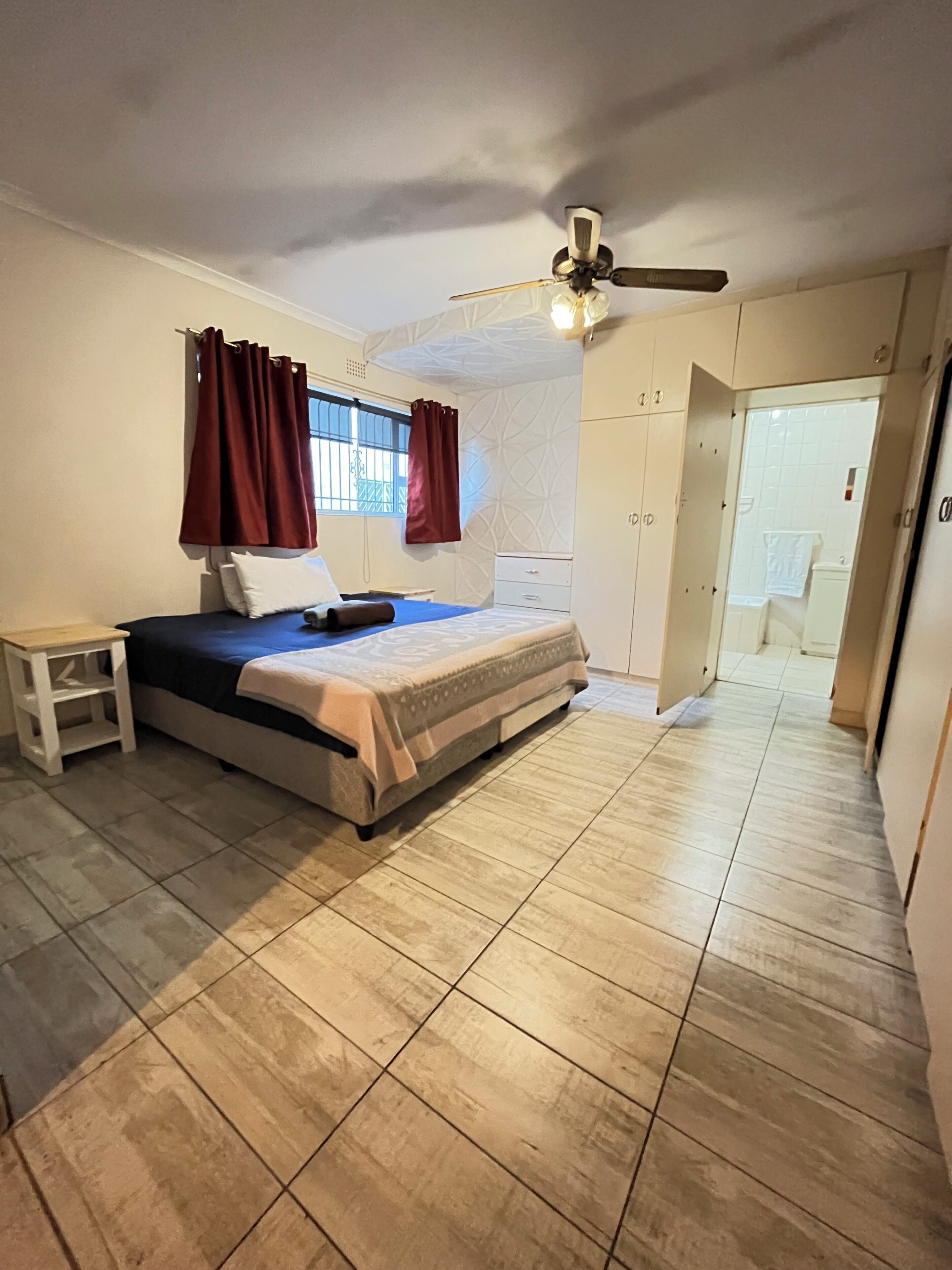Une chambre à coucher comprenant un lit, une table de chevet, un ventilateur de plafond et une armoire.