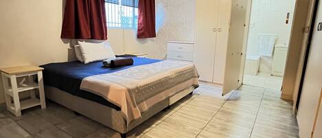 Un dormitorio con cama, mesita de noche, ventilador de techo y armario.