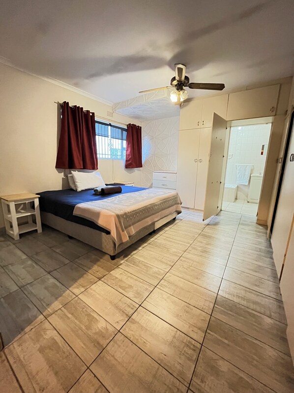 Une chambre à coucher comprenant un lit, une table de chevet, un ventilateur de plafond et une armoire.