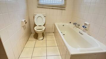 Un baño con inodoro, bañera y ventana con persianas.