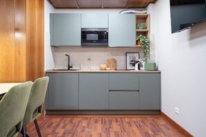 Cozinha compacta com armários cinza, micro-ondas, pia e bancada pequena com uma planta e um porta-retrato.