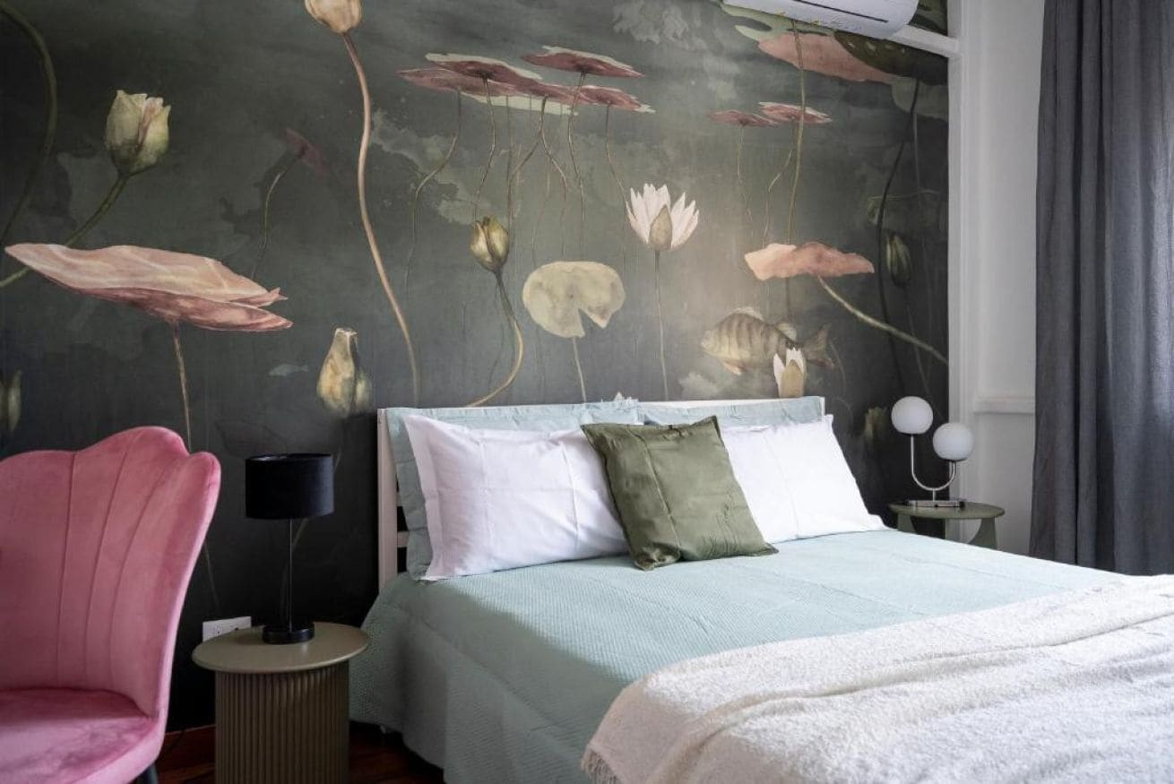 Een slaapkamer met een bed, kussens, een bedlampje, een stoel en een muurschildering.