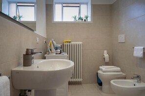 Casa de banho moderna com uma grande pia, sanita, bidé e janela com plantas.
